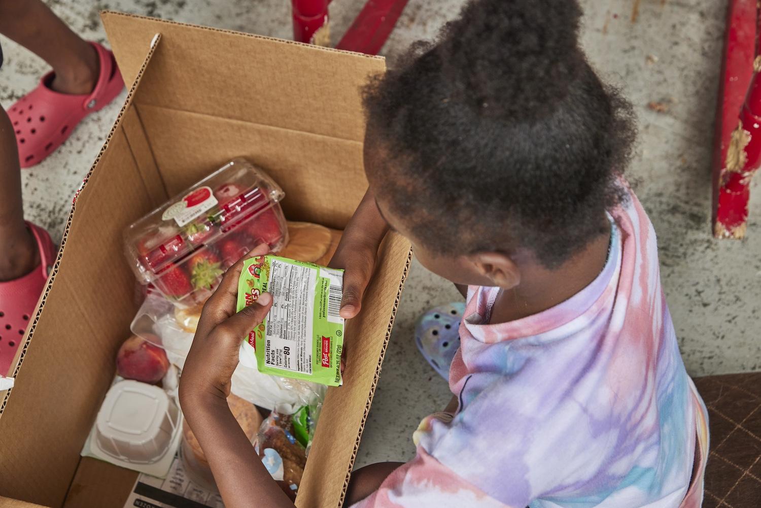 A child opens a box of food from the summer meal program. 